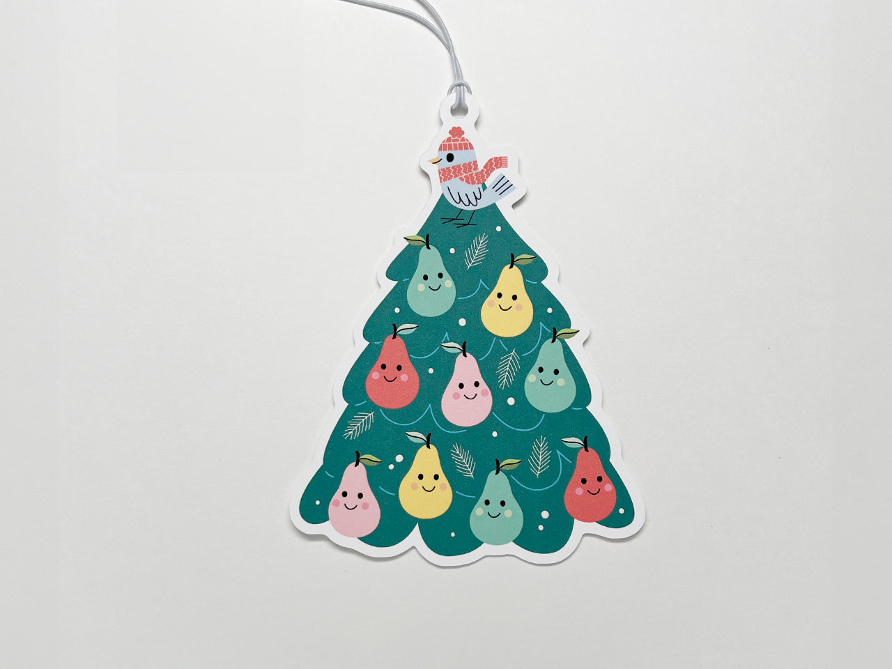A colorful Christmas tree-shaped gift tag featuring a whimsical design of smiling pears in pink, green, red, and yellow, topped with a partridge wearing a red hat and scarf. The tag has a white string attached for use with holiday gifts.