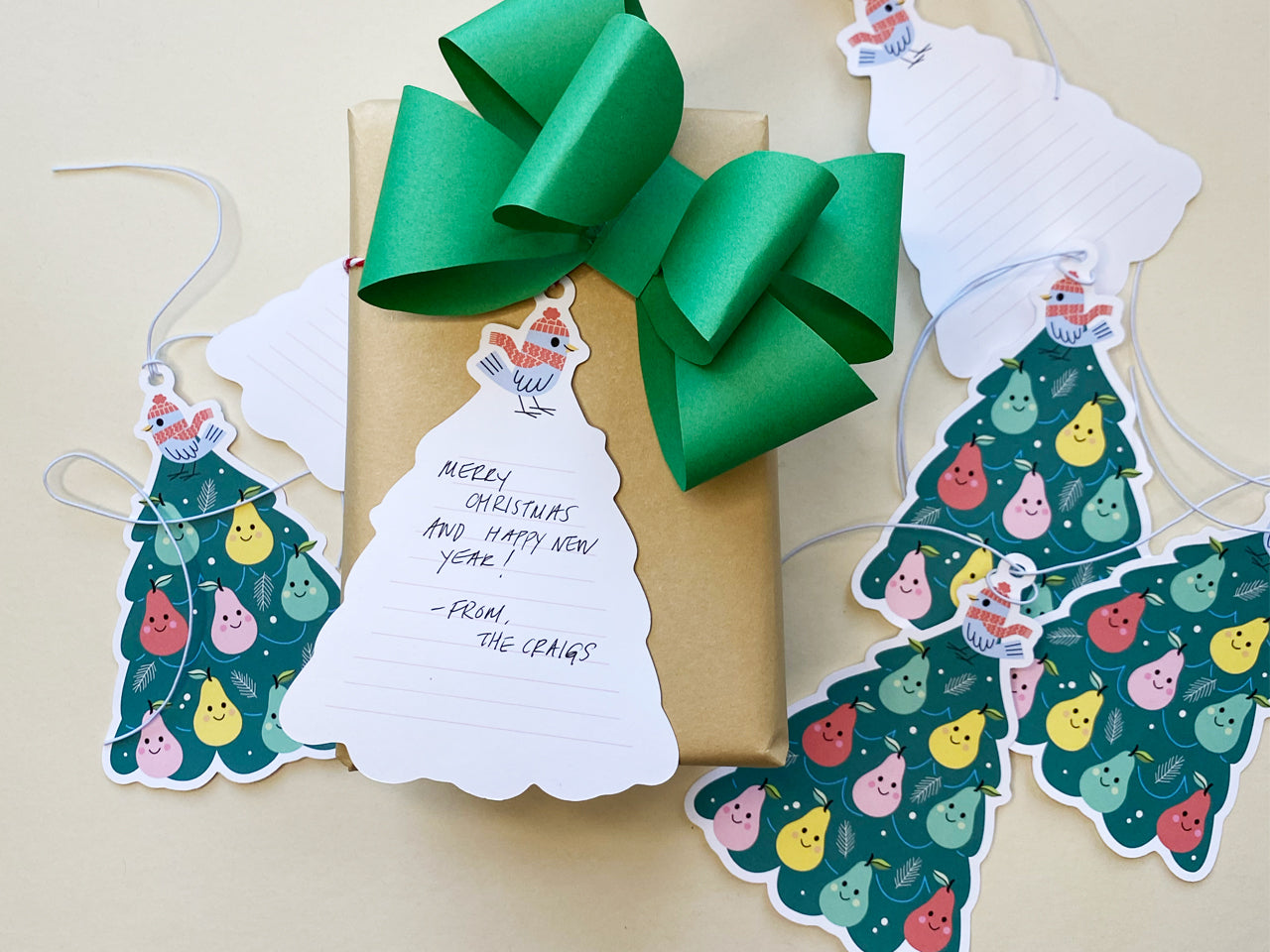 A festive Christmas gift with a green bow and a whimsical Partridge in a Pear Tree gift tag featuring space for a handwritten message. Other tags with smiling pears are scattered nearby, creating a playful and charming holiday gift presentation.