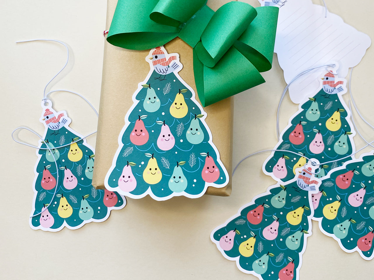 A set of colorful Christmas gift tags featuring a whimsical partridge in a pear tree design. The gift tags are shaped like Christmas trees, decorated with smiling pears in various colors, and topped with a bird wearing a red winter hat and scarf.
