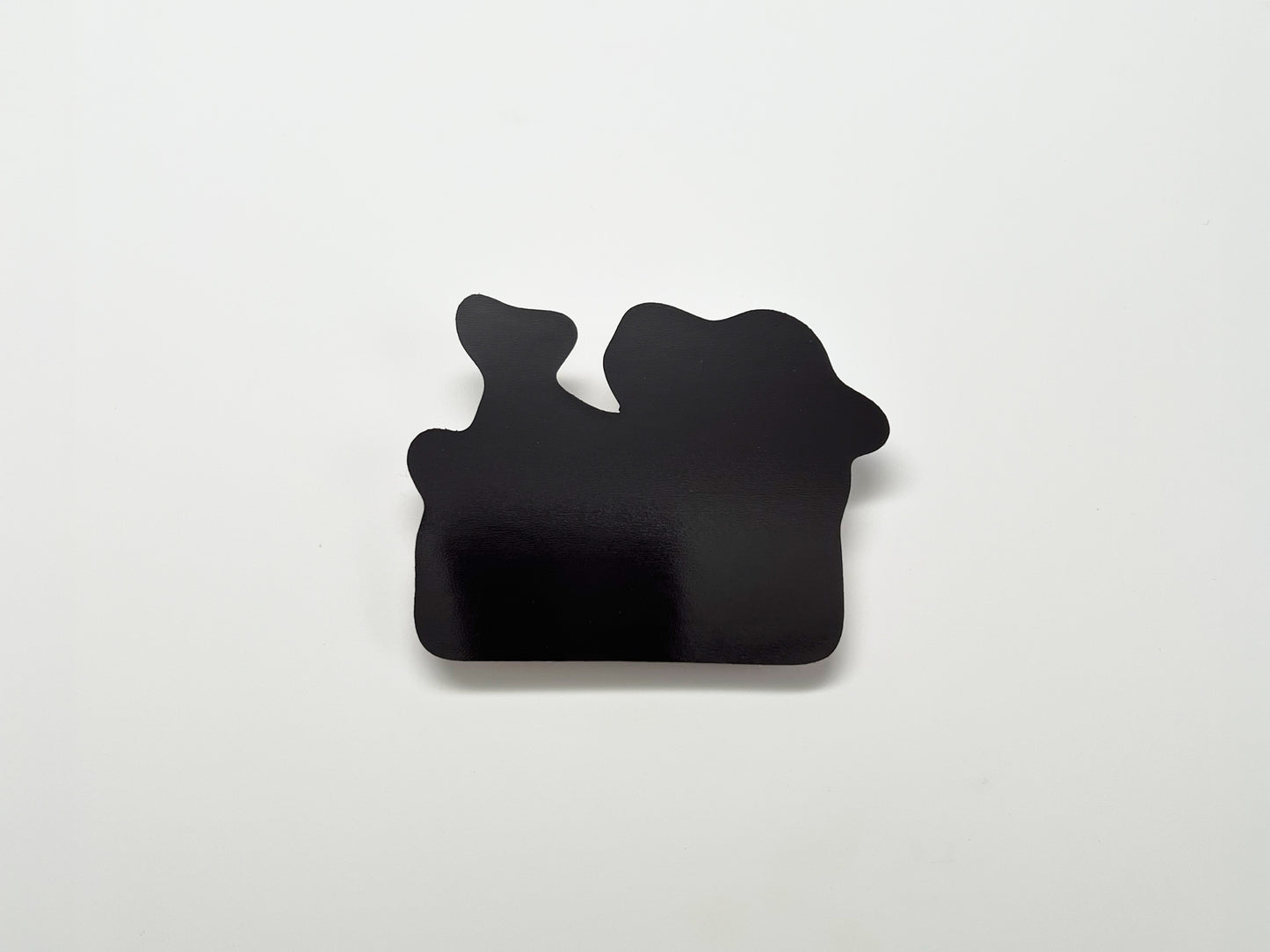 Back view of a handmade die-cut magnet, showing its solid black magnetic surface in an irregular shape. Designed to securely attach to metal surfaces like refrigerators, lockers, or filing cabinets.