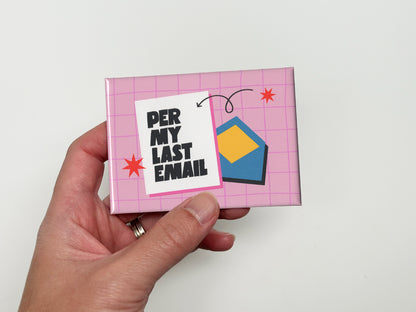 Hand holding a glossy pink magnet with a light pink grid background, bold black text that reads “Per My Last Email,” and a blue envelope illustration with red star accents.