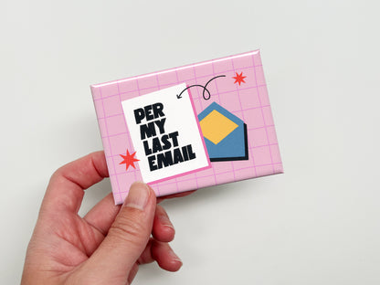 Hand holding a rectangular pink magnet with a light pink grid pattern, bold black text that reads “Per My Last Email,” and a blue envelope illustration with small red star accents and a curved arrow detail.