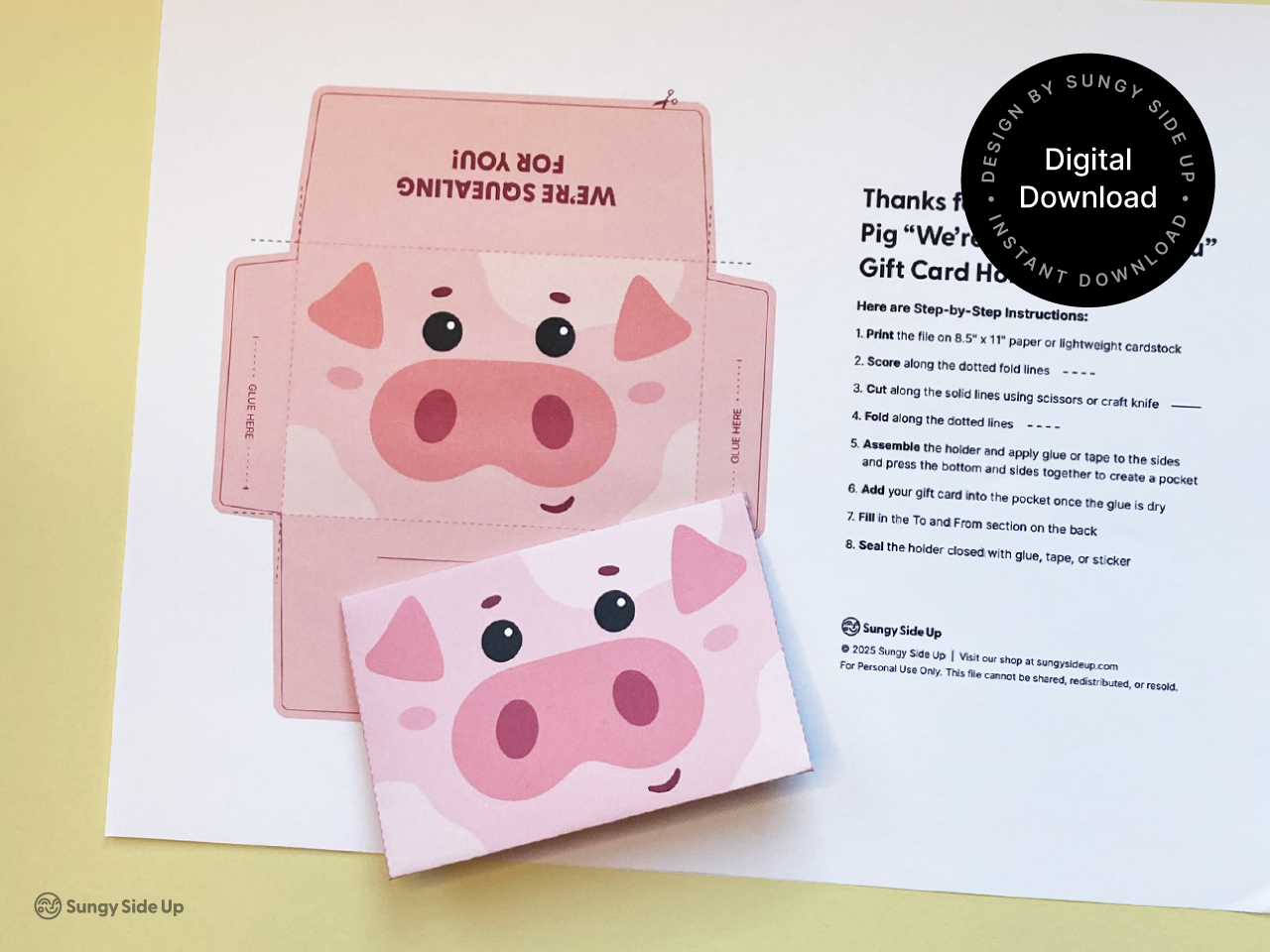A printable pig gift card holder template is displayed on a yellow surface next to a fully assembled pig gift card holder. The template features a pink cartoon pig face with large eyes, ears, and a snout, along with cut, fold, and glue lines for DIY assembly. The design is a digital download from Sungy Side Up, including step-by-step instructions for creating an animal-themed gift card holder for birthdays, parties, and special occasions.