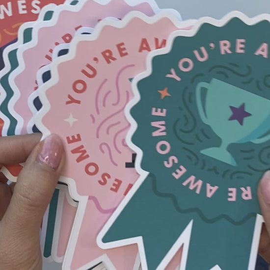 Multi-colored ribbon note cards showing teal, pink, orange, and indigo. Woman writing on the back of one note card to send a note of encouragement to a teacher.