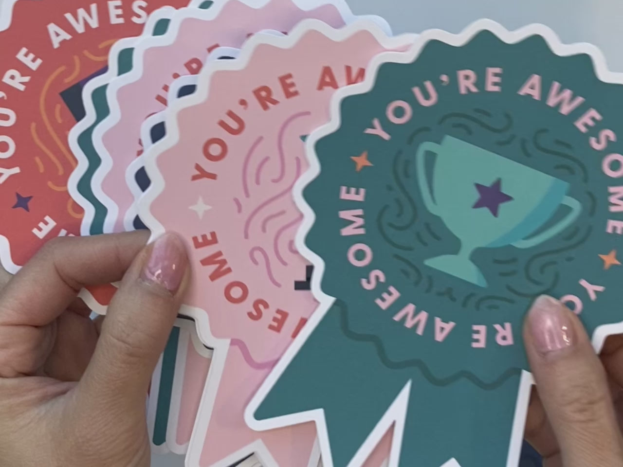 Multi-colored ribbon note cards showing teal, pink, orange, and indigo. Woman writing on the back of one note card to send a note of encouragement to a teacher.