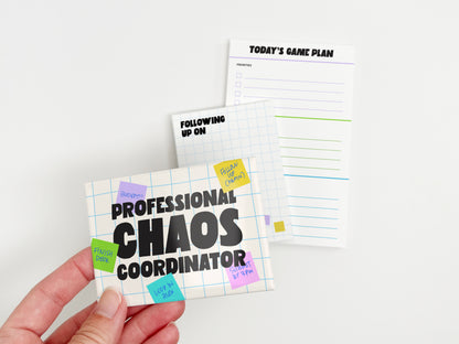 Hand holding a Professional Chaos Coordinator magnet with matching follow-up notepad and Today's Game Plan task notepad in the background.