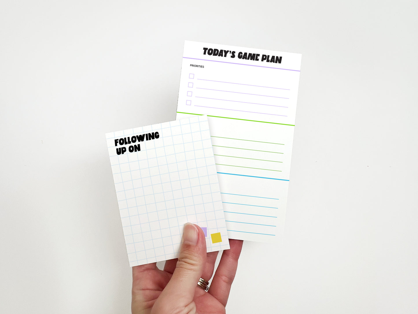 Hand holding the Following Up On mini notepad and Today's Game Plan task notepad from the Professional Chaos Coordinator stationery gift set.
