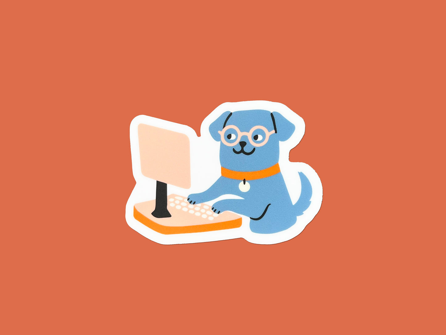 Illustrated matte die cut vinyl sticker of a blue dog wearing round glasses and an orange collar, sitting upright and typing on a peach-colored desktop computer. Sticker has a white border and is centered on a solid orange background.