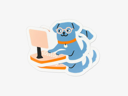 Small stack of matte die cut vinyl stickers featuring an illustrated blue dog wearing round glasses and an orange collar, sitting upright and typing on a peach-colored desktop computer. Stickers have white borders and are photographed on a white background.