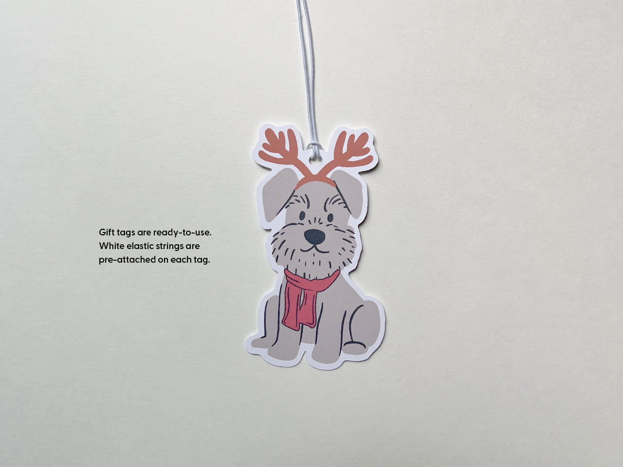 A reindeer Schnauzer holiday gift tag with a white elastic string pre-attached, ready to use. The handmade tag features a cute gray Schnauzer wearing reindeer antlers and a red scarf, perfect for Christmas gift wrapping and pet-themed holiday decor.