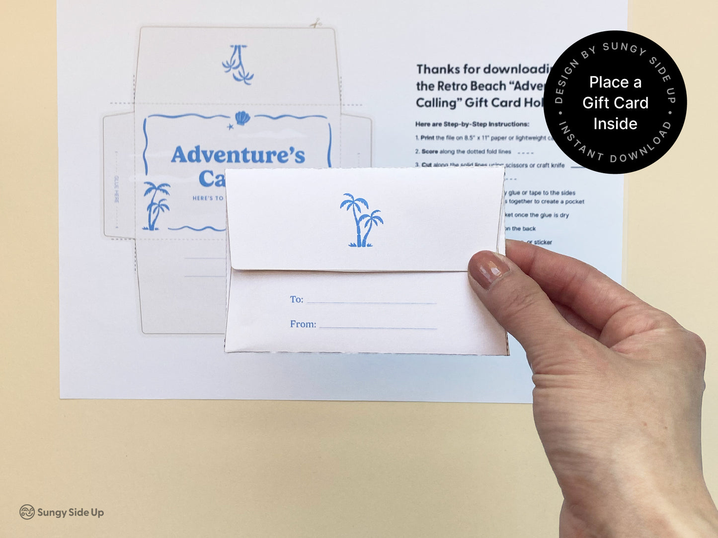 A person holds a folded printable gift card holder with a palm tree illustration, designed in a retro beach theme. Behind the hand is a printed instruction sheet and an unfolded version of the same gift card holder template, featuring ocean-themed graphics in blue. This DIY gift card envelope is part of a digital download bundle for thank you gifts, graduations, and special occasions. Ideal for summer events, beach parties, and coastal-themed celebrations.