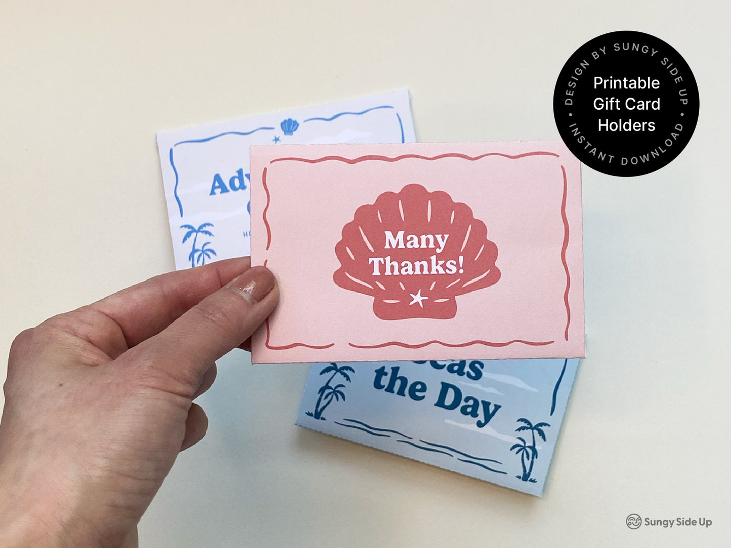 A hand holds a folded pink printable gift card holder with a red seashell illustration and the words "Many Thanks!" in the center. In the background, two additional printable gift card sleeves with beach-themed designs are partially visible—one in light blue and the other in white and blue. These retro-style digital gift card envelopes are part of an instant download bundle, ideal for thank you gifts, coastal-themed celebrations, beach party favors, and summer gifting occasions.