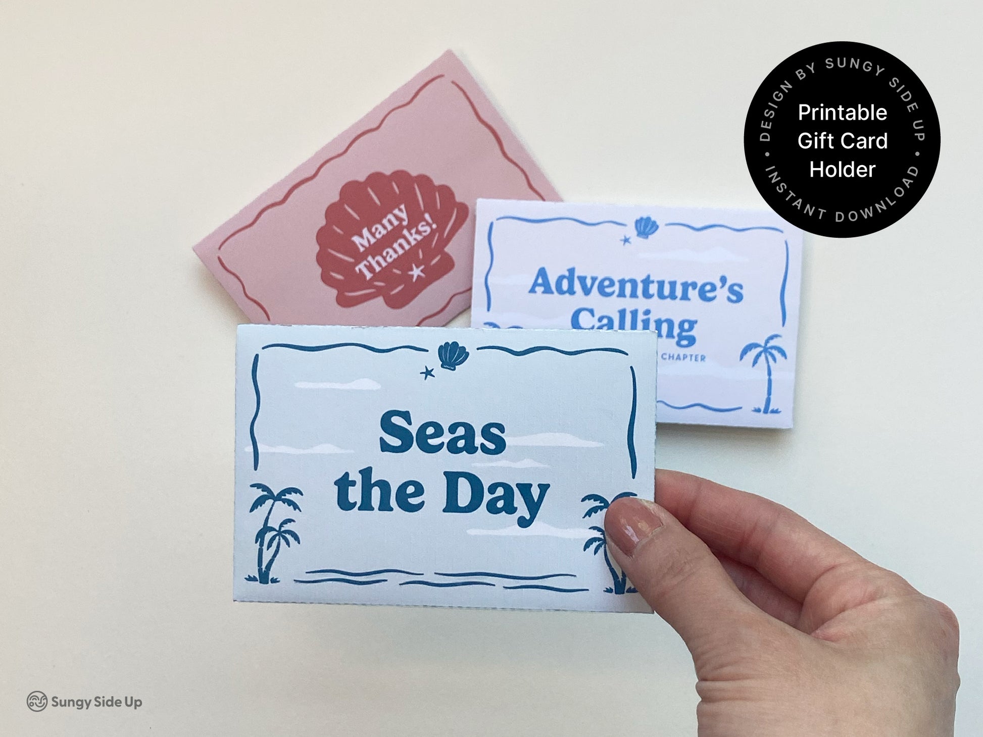 A hand holds a folded light blue printable gift card holder with a retro beach design that says "Seas the Day." In the background, two other coordinating card sleeves are visible—one in pink with a red seashell and the words "Many Thanks!" and another in white and blue that says "Adventure’s Calling." All three are part of a themed digital gift card holder bundle, ideal for thank you gifts, graduations, summer events, and coastal-themed celebrations. Instant download and easy to print.