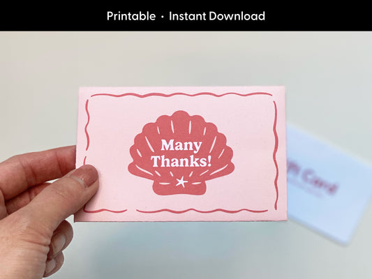 Hand holding a printable retro-style gift card holder in pink and red colors with a seashell graphic on the front. The design features a beach or coastal theme with a simple, vintage aesthetic. The card holder is made of paper and is shown fully assembled, intended for use with standard gift cards. The background includes a blurred gift card to show scale and usage. Ideal for thank you gifts, summer parties, beach weddings, or coastal-themed celebrations. Instant download format.