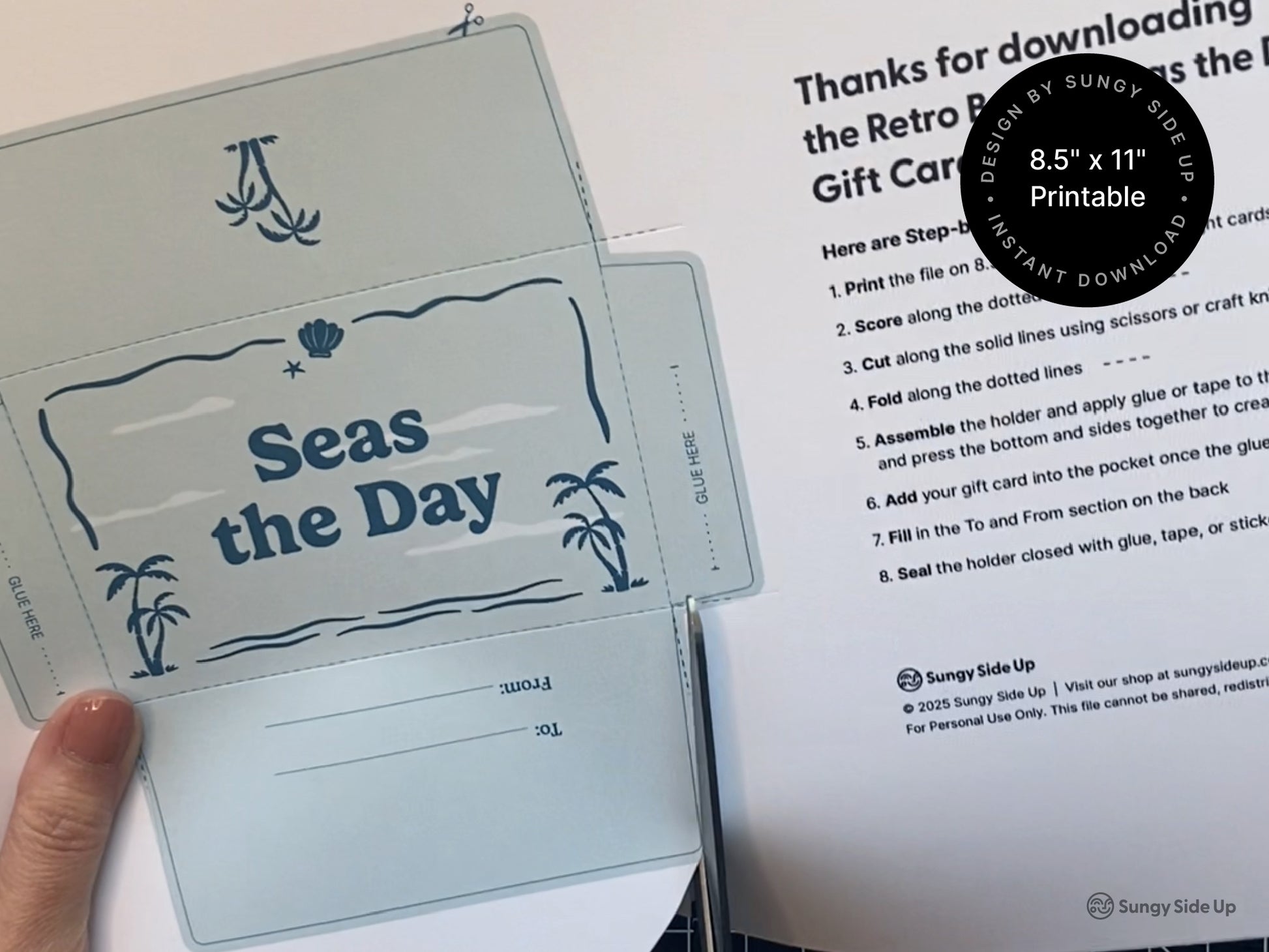 Person holding a printed template for a gift card holder with a tropical beach theme and the phrase Seas the Day in blue text. The sheet includes fold lines and assembly instructions printed on standard 8.5 by 11 inch paper. A separate instruction page is visible in the background. This DIY project is a digital download designed for easy at home printing cutting and gluing. Perfect for creating thoughtful handmade gift card envelopes for summer thank you or birthday occasions.