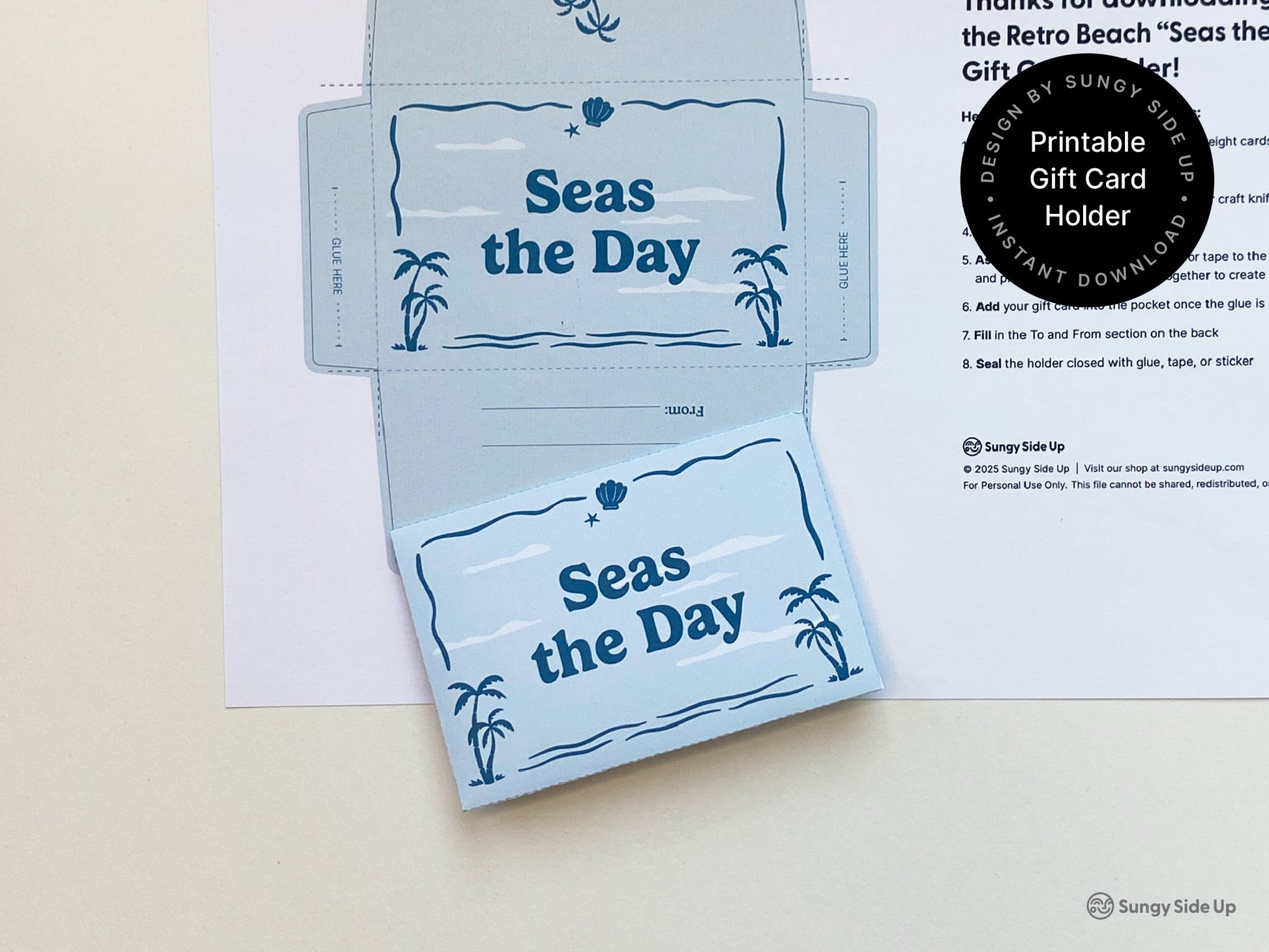 Flat lay of a printable gift card holder with a retro beach theme featuring palm trees and ocean elements in blue tones. One version is fully assembled while the other is uncut and placed on a printed instruction sheet. The design includes a pocket for inserting a gift card and a section to write to and from. Ideal for summer gifts thank you presents or birthdays. Instant download project for DIY gifting that is simple to print cut fold and assemble at home.