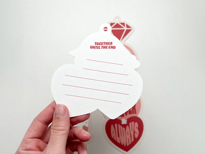 A close-up of the back of a heart-shaped retro-style gift tag with the phrase Together Until the End printed at the top in red. The tag has pre-punched holes for attachment and horizontal red lines for writing.