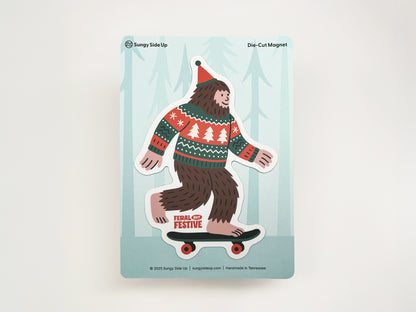 Die-cut Christmas Sasquatch magnet featuring Bigfoot on a skateboard wearing a festive sweater and Santa hat, displayed on Sungy Side Up backing card.