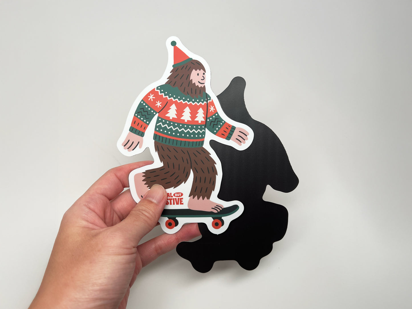 Holiday Bigfoot magnet front and black magnetic backing shown together, handmade festive Sasquatch fridge magnet by Sungy Side Up.