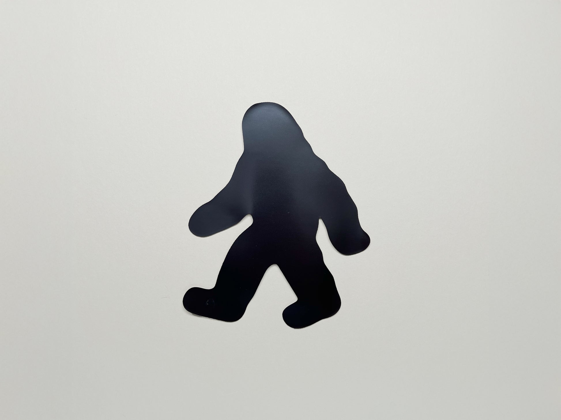 Back side of die-cut Bigfoot magnet in a walking pose; strong black magnetic backing shown for handmade Sasquatch fridge magnet by Sungy Side Up—fun and functional gift for cryptid lovers and outdoor adventurers.
