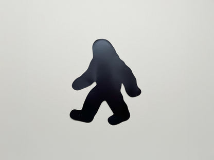 Back side of die-cut Bigfoot magnet in a walking pose; strong black magnetic backing shown for handmade Sasquatch fridge magnet by Sungy Side Up—fun and functional gift for cryptid lovers and outdoor adventurers.