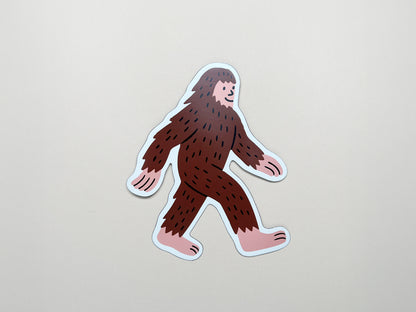 Cute die-cut Sasquatch magnet featuring a smiling brown Bigfoot walking with pink hands and feet; handmade quirky fridge magnet by Sungy Side Up—perfect for whimsical gifts, cryptid collectors, and fun home décor.