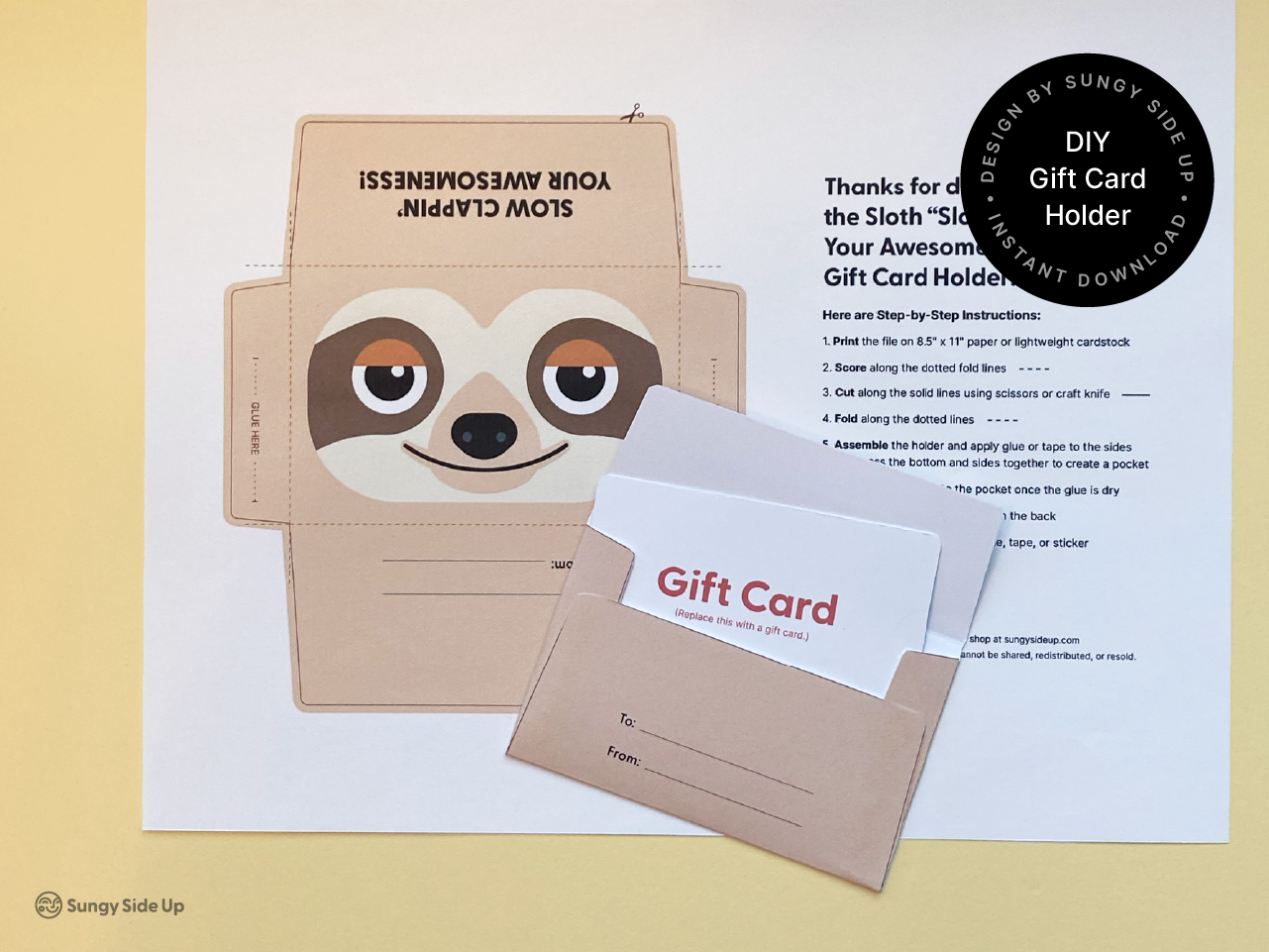 A digital sloth gift card holder template printed on paper, shown next to a fully assembled version of the holder. The design features a happy sloth with brown and beige coloring and fold lines for easy assembly. The finished product is a functional envelope for holding a gift card, making it a creative and personal way to package a present. The scene shows both the printed template and a completed version of the holder, ready for use.