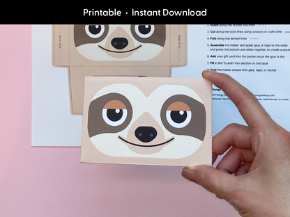 A hand holds a completed sloth gift card holder made from a printable template. The front features a smiling cartoon sloth with warm brown and beige tones. The background shows the flat printable sheet with cutting and folding guides. The image highlights the finished product’s size and quality, making it a great last-minute gift wrap option for kids, teachers, or anyone who loves animals and handmade gifting ideas.