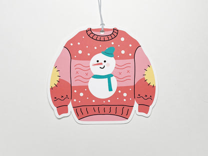 A single pink Christmas sweater-shaped gift tag featuring a smiling snowman with a teal scarf and hat. The whimsical design includes yellow elbow patches and festive snowflakes, making it a fun addition to any holiday gift.