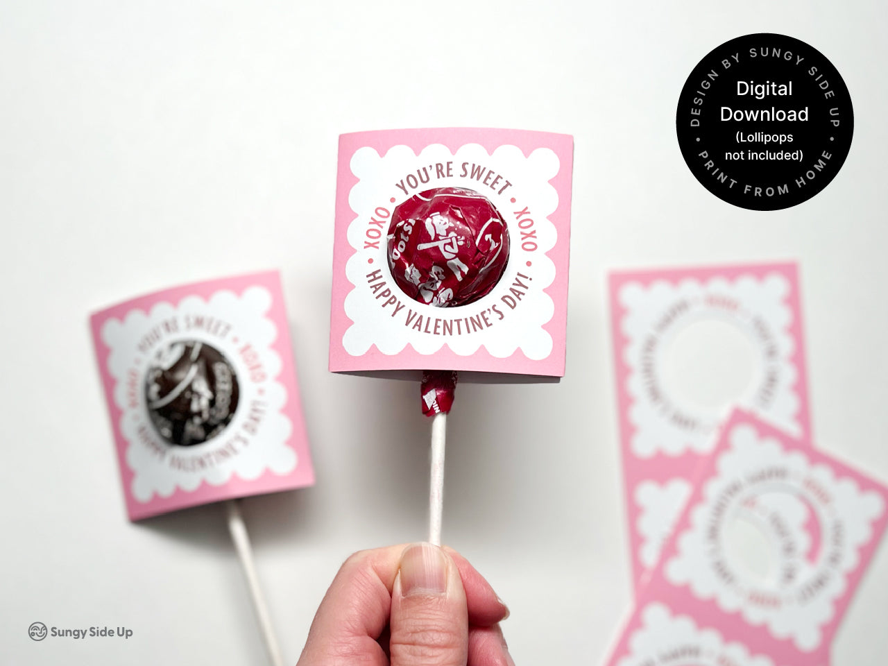 Close-up of a pink assembled Valentines Day lollipop candy holder featuring a scalloped design with a lollipop inserted. Printing these printables at home are ideal for creating unique and fun gifts and classroom exchanges for Valentines Day.