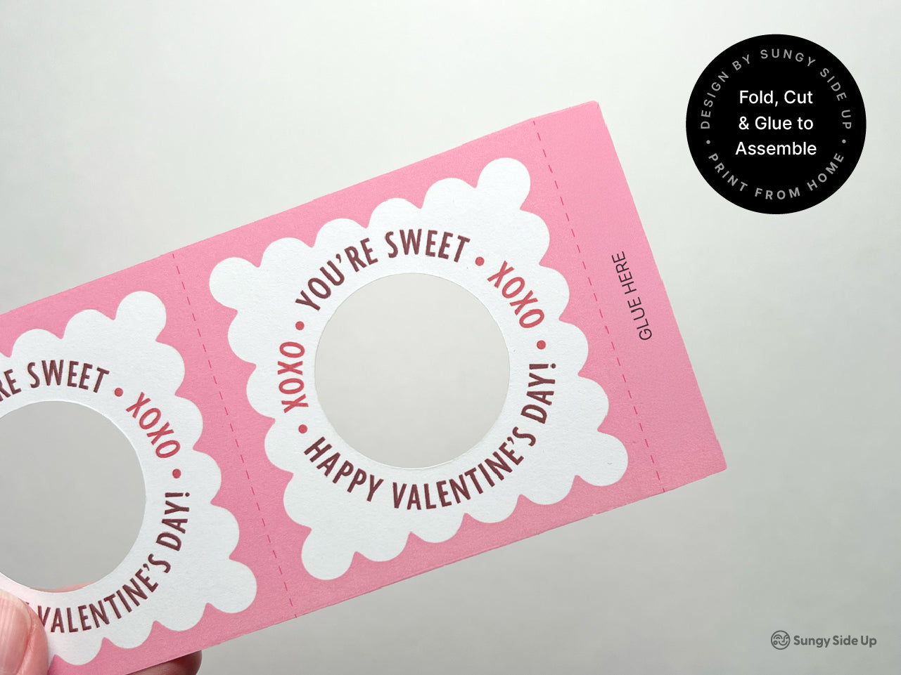 A close-up of a pink printable Valentines Day lollipop holder, showcasing scalloped edges and a circular cutout for the lollipop. Designed for easy cutting, folding, and gluing, perfect for DIY Valentine crafts, treats, and classroom parties.