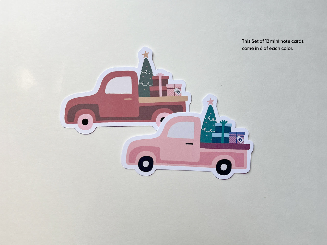 Two die-cut vintage truck mini note cards, one in burnt orange and the other in pink. Both trucks carry festive Christmas trees and gift boxes, displayed on a light background.