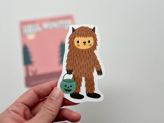 A handmade die-cut Bigfoot Halloween magnet shaped like a cute woodland creature holding a teal jack-o’-lantern candy bucket. Perfect spooky season fridge décor for cryptid lovers, sasquatch fans, and quirky Halloween gifts, made in Tennessee with a whimsical, playful design.