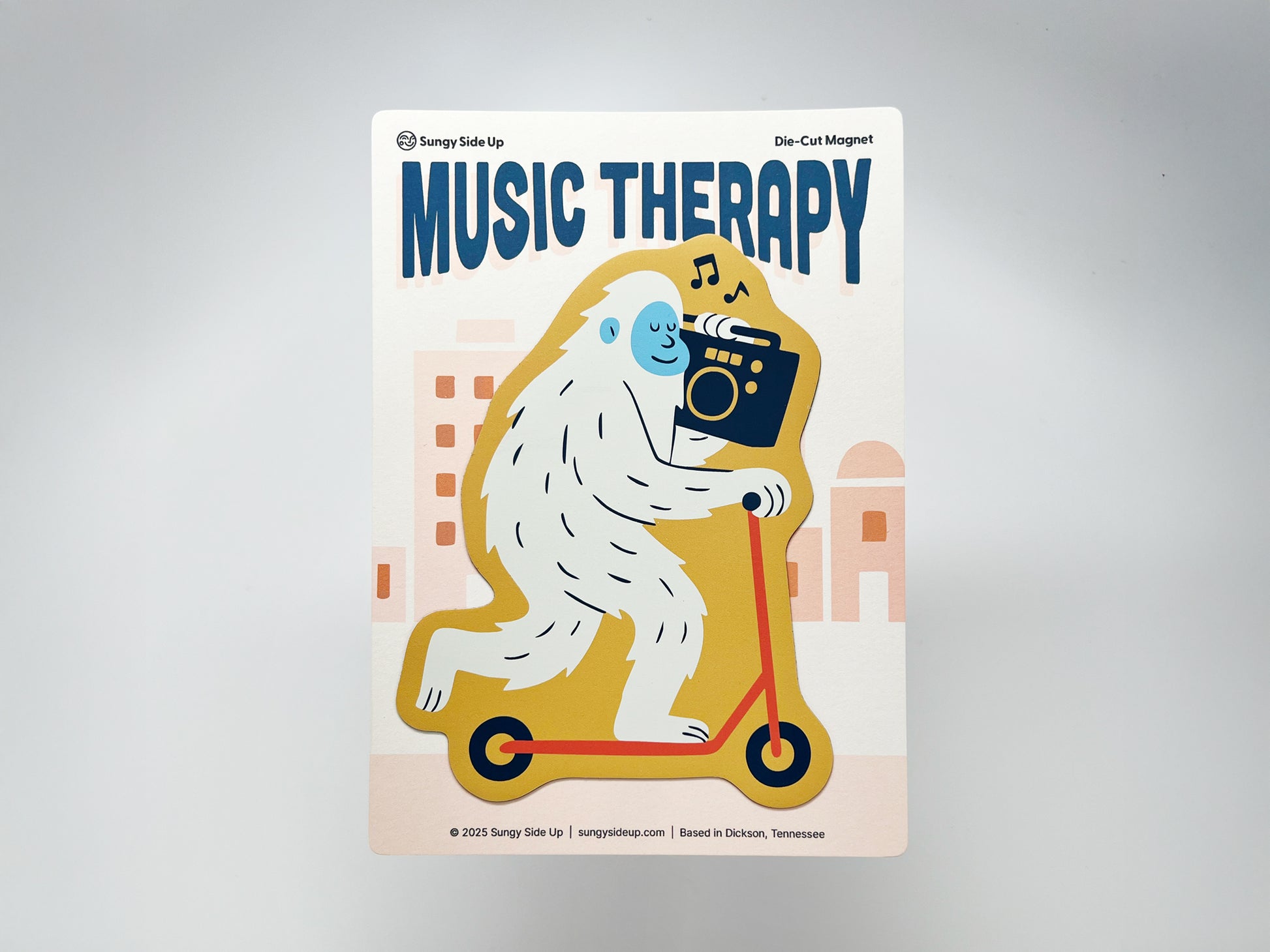 Die-cut fridge magnet featuring a quirky white yeti riding a yellow scooter while holding a boombox with music notes above. The text “Music Therapy” appears at the top. Fun novelty magnet gift for music lovers, scooter fans, and quirky home or kitchen decor.