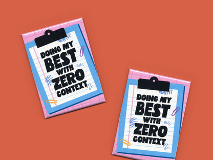 Two “Doing My Best With Zero Context” magnets displayed on a reddish-orange background. The magnets feature a pink grid pattern, blue clipboard illustrations, and bold black text on lined paper.