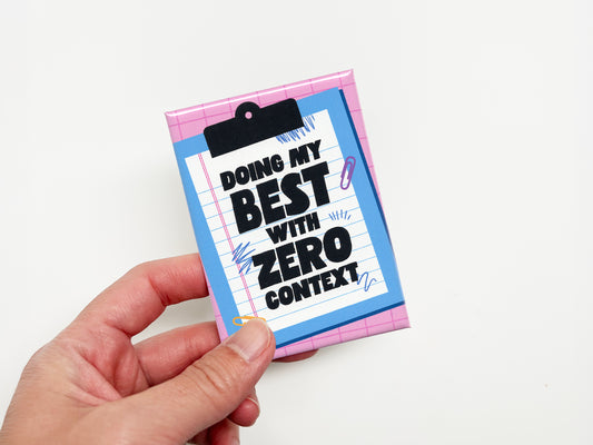 Hand holding a rectangular magnet with a pink grid background and a blue clipboard illustration holding lined paper. Bold black text reads “Doing My Best With Zero Context.”